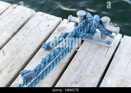 Poller mit gebundenen blau nautischen Seil montiert auf weißen Holzmole Liegeplatz, yacht Marina Sicherheitsausrüstung Stockfoto