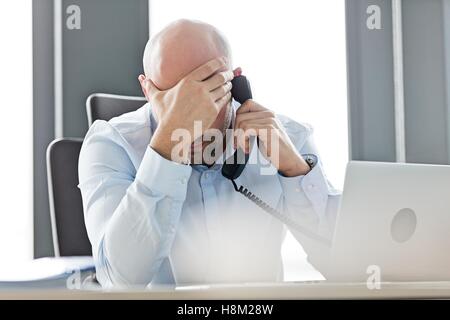 Mitte adult Geschäftsmann mit Festnetz-Telefon am Schreibtisch im Büro müde Stockfoto