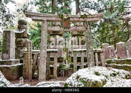 Koyasan, Japan, Okunoin Friedhof. Stein Torii-tor vor drei gorinto, fünf-beringte Türmen. Zedernwald Hintergrund. Etwas Schnee. Stockfoto