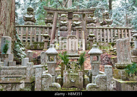 Koyasan, Japan, Okunoin Friedhof. Stein Torii und Laternen, hinter, dass Grab Gedenkstätten und gorinto fünf beringt Türme im zedernwald Hintergrund. Stockfoto