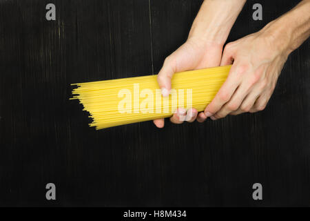 Spaghetti in Händen flach zu legen. Draufsicht Bündel von rohen Spaghetti in männlichen Händen auf schwarzem Holz Vintage Tisch Stockfoto