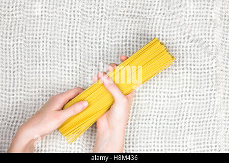 Rohe Spaghetti in weiblichen Händen flach zu legen. Draufsicht der Bund ungekochte Spaghetti auf leichte Leinwand Hintergrund Stockfoto