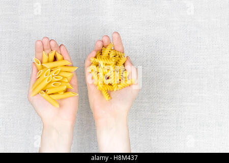 Handvoll Teigwaren flach zu legen. Weibliche Hände halten Haufen rohe Fussilli und Penne-Nudeln auf weiße Leinwand Hintergrund Stockfoto