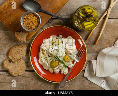 Hausgemachte Deutsche Kartoffelsalat mit Frankfurter Würstchen auf einem rustikalen Tisch mit Brot, Gurken und Senf Samen. Stockfoto