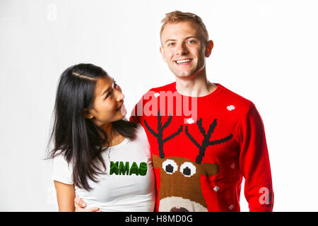 Porträt von glücklich Multi ethnischen paar Weihnachten Jumper im Studio tragen, während sich gegenseitig auf der Suche Stockfoto