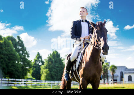 Nachdenklich gut gekleideter Mann saß auf Pferd gegen bewölktem Himmel Stockfoto