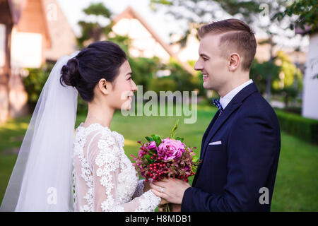 Seitenansicht des Lächelns Hochzeitspaar halten Blumenstrauß auf dem lawn Stockfoto