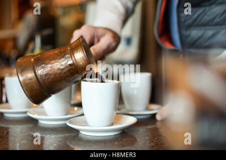 Man gießen Türkische/griechischen Kaffee aus einem Topf in einen weißen Porzellan Schale Stockfoto