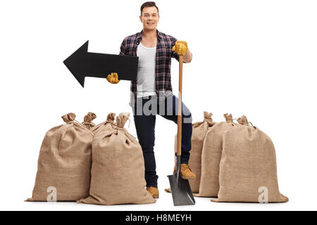 Landwirt stehend zwischen Sackleinen Säcke mit einer Schaufel und ein Pfeil links isoliert auf weißem Hintergrund Stockfoto