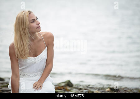 Blonde Frau kauert in der Nähe eines Flusses Stockfoto