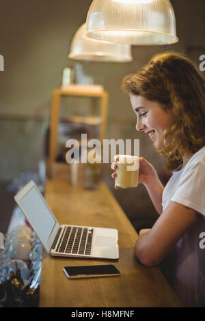 Schöne Mechaniker Kaffeetrinken während mit Laptop am Schalter Stockfoto