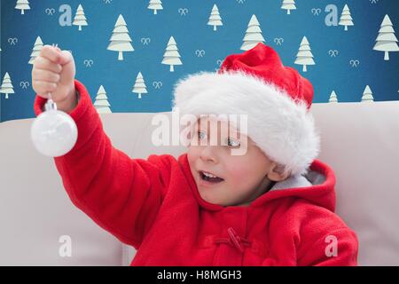 Kleiner Junge in Weihnachtsmütze hält eine Christbaumkugel Stockfoto