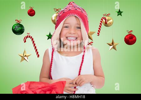 Glückliches Mädchen in gestrickte Wollmütze lächelnd gegen digital generierte Weihnachts-Dekoration Stockfoto