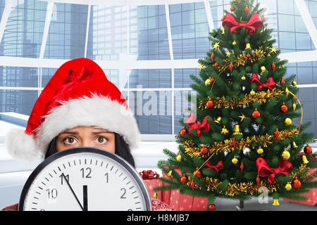 Frau in Nikolausmütze versteckt sich hinter einer Uhr Stockfoto