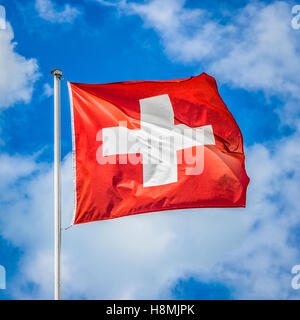 Klassische Ansicht der Nationalflagge der Schweiz winken im Wind vor blauem Himmel mit Wolken an einem sonnigen Tag Stockfoto