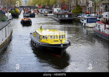 Ein Polizeiboot führenden Nachtschwärmer feiern Geburtstag des Königs in Booten in Amsterdam, Niederlande. Stockfoto