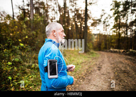 Senior-Läufer in der Natur mit Smartphone und Kopfhörer. Stockfoto