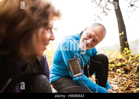 Senior-Läufer in der Natur, Schnürsenkel zu binden. Mann mit Smartphone. Stockfoto