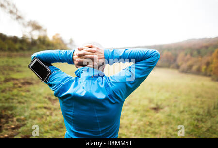 Senior Läufer mit Smartphone Dehnung zu tun. Herbst Natur. Stockfoto