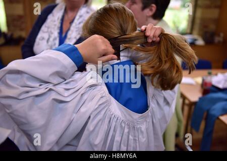 Mädchen Chorknabe bindet Haar. Chorknaben an Soutane passend und Proben für Abendandacht. Stockfoto