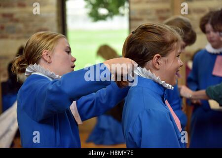 Chorknaben an Soutane passend und Proben für Abendandacht. Mädchen Chorknabe bindet Haar von einem anderen Mädchen Chorsänger. Stockfoto