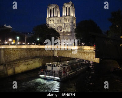 Die Kathedrale Notre Dame ist nachts beleuchtet und ein Passagierboot entlang der seine, Paris, Frankreich. Stockfoto