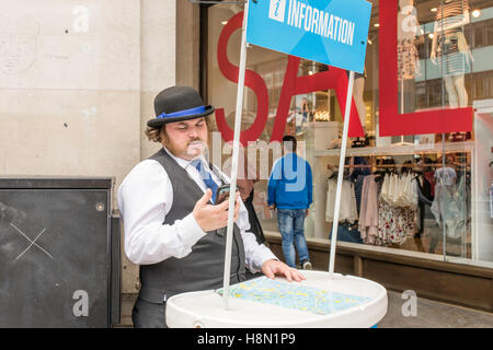 Ein Reiseführer, sein Handy zu betrachten, steht er hinter einer Theke mit einer Karte von London, bereit, Touristen und Besucher brauchen Führung zu unterstützen. Stockfoto