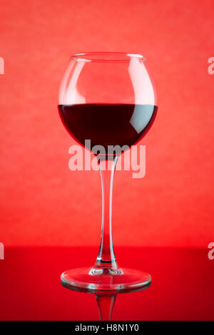 Rotweinglas vor rotem Hintergrund. Am Tisch mit Reflexion Stockfoto