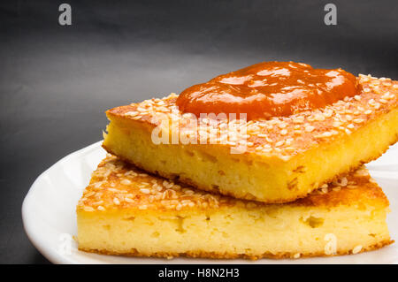 Stück Käsekuchen mit Sesam und Marillenmarmelade auf schwarzem Hintergrund Stockfoto