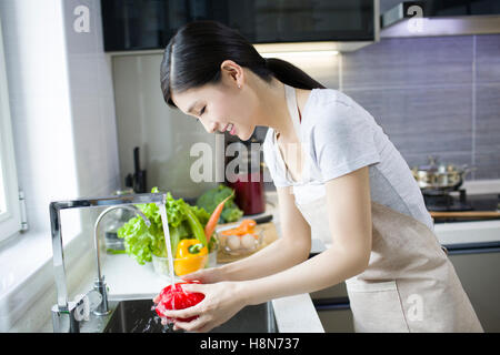 Glückliche junge Chinesin Waschen von Gemüse in der Küche Stockfoto