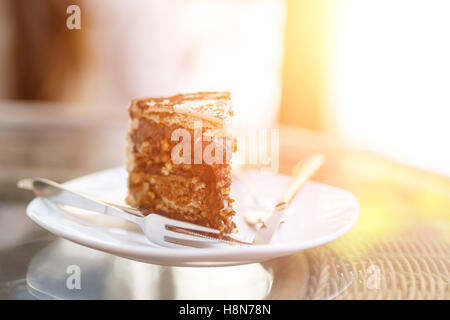 Stück Schokoladenkuchen auf Teller mit Gabel und Messer auf Glastisch Stockfoto