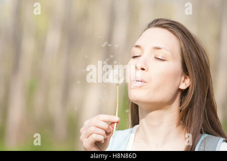 Junge Frau bläst Blume Löwenzahn im Frühling Stockfoto