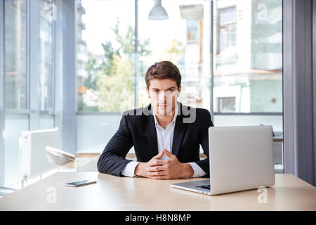 Ernst junger Geschäftsmann mit Laptop im Büro am Tisch sitzen Stockfoto