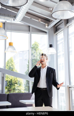 Happy begeistert junge Unternehmer stehen und telefonieren mit Handy im café Stockfoto