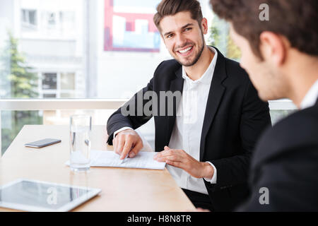 Zwei fröhliche junge Geschäftsleute sprechen und arbeiten mit Dokumenten in office Stockfoto