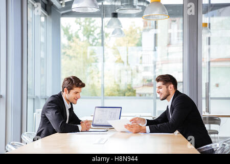 Zwei glückliche junge Geschäftsleute arbeiten zusammen mit Laptop auf Business-Meeting im Büro Stockfoto
