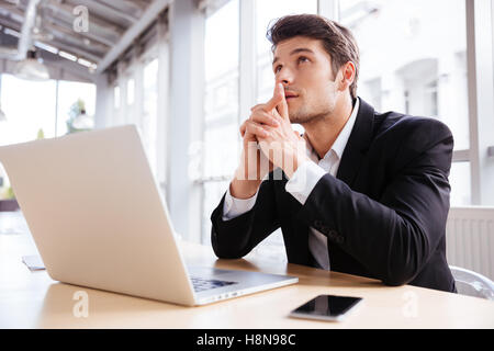 Nachdenklicher junger Geschäftsmann denken und mit Laptop im Büro Stockfoto