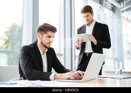 Zwei junge Unternehmer arbeiten mit Notebook und Tablet konzentriert im Büro Stockfoto