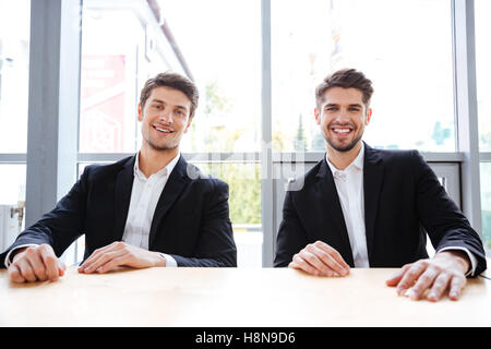 Zwei fröhliche erfolgreiche Jungunternehmer am Tisch im Büro Stockfoto