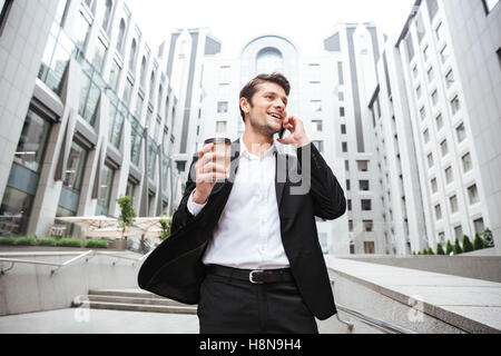 Glückliche junge Geschäftsmann telefonieren mit Handy und Kaffeetrinken in der Nähe von Business-center Stockfoto