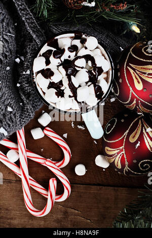 Emaille Tasse heißen Kakao zu Weihnachten mit Marshmallows und garniert mit Schokoladensauce.  Umgeben von einem Schal und Süßigkeiten, Stockfoto