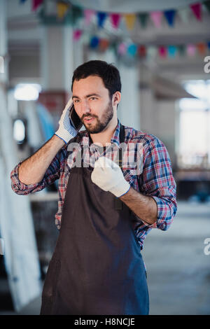Austausch von Ideen. Glücklich Jüngling telefonieren mit dem Handy stehen in seiner Werkstatt Stockfoto