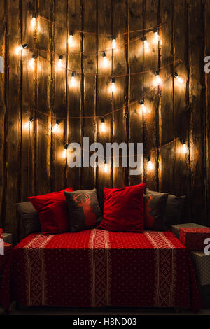 Holzzimmer in rustikalen Haus mit Holzwand und Designer-Lampen, geschmückten Platz für Sitz. Rot grau Kissen. Stockfoto