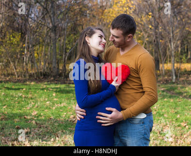 Glücklich schwanger paar umarmen einander. Sie hält ein Kuscheltier in Form eines Herzens. Sie sehen glücklich. Herbstzeit Stockfoto