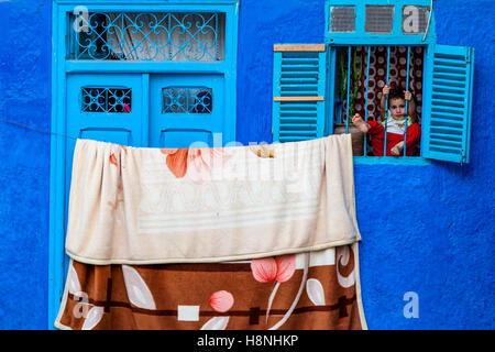 Ein kleines Kind sitzt hinter dem Fenster Bars von einem Haus in der Medina, Ouarzazate, Marokko Stockfoto