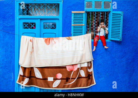 Ein kleines Kind sitzt hinter dem Fenster Bars von einem Haus in der Medina, Ouarzazate, Marokko Stockfoto