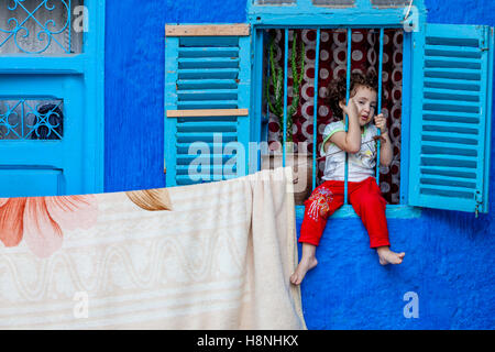 Ein kleines Kind sitzt hinter dem Fenster Bars von einem Haus in der Medina, Ouarzazate, Marokko Stockfoto