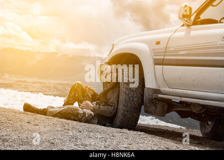 Mann sitzt auf einem Berg neben dem Rad ein SUV und Rest. Vor dem Hintergrund der Schnee die Berge. Die Höhe von 3000 Meter. Altai, Russland. Stockfoto