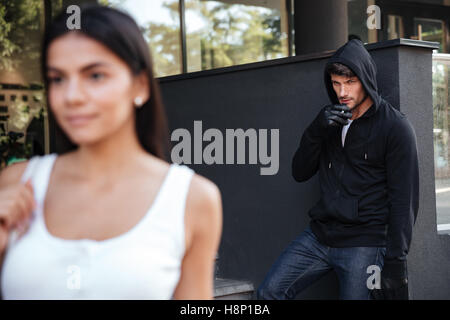 Gefährlicher Mann Räuber Rauchen und mit Blick auf die junge Frau zu Fuß in die Stadt Stockfoto