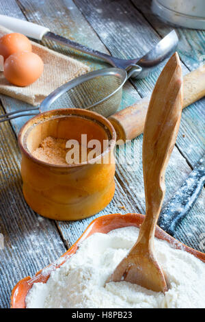 Der hölzerne Löffel stecken die Keramikschale mit Mehl, ein Glas mit Adyge Salz, Eiern, Nudelholz, Metallsieb und einer Kelle. Stockfoto